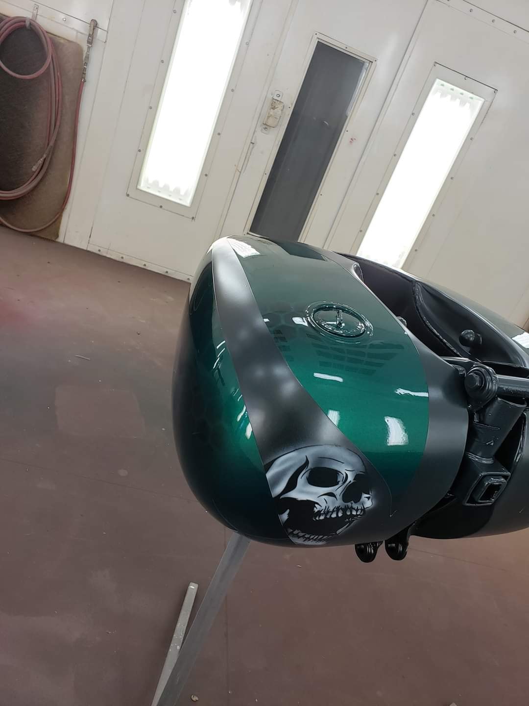 Green and black motorcycle tank with skull airbrush in paint booth